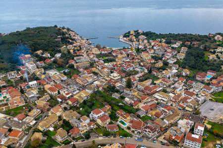 Detailed aerial drone shot of Kassiopi town center showing dense architecture, the main harbor entrance, and green vegetation surrounding the resort in northern Corfuの写真素材