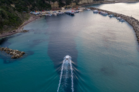 Aerial view of the small fishing harbor of Agios Stefanos Avliotes at sunset, featuring stone breakwaters, moored boats, and calm turquoise waters on the northwest coast of Corfu island, Greece.の写真素材