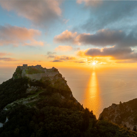 Aerial view of Angelokastro Byzantine castle ruins silhouetted against golden sunset with bright sun reflection path on Ionian Sea water in Corfu island, Greece, dramatic scenery.の写真素材