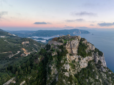 Aerial panoramic view of Angelokastro castle ruins on cliff and Paleokastritsa bay coastline in Corfu Greece. Scenic summer landscape of Ionian sea, green mountains and historic fortress at sunsetの写真素材
