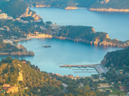 Aerial view of Alipa Port in Paleokastritsa, Corfu, Greece, featuring sailboats and yachts docked in the turquoise marina surrounded by lush green hills during summerの写真素材