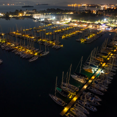 Aerial night view of Gouvia Marina in Corfu island Greece featuring illuminated piers with docked luxury yachts and sailboats in the harbor with dark water reflectionsの写真素材