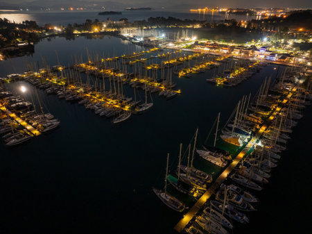 Top down aerial night shot of organized rows of sailboats and yachts moored at the pier in Corfu marina Greece illuminated by golden streetlightsの写真素材