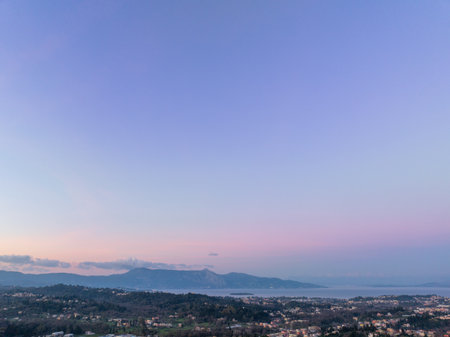 Soft purple and pink sunset sky over the distant mountains and calm sea viewed from high above the green inland hillsの写真素材