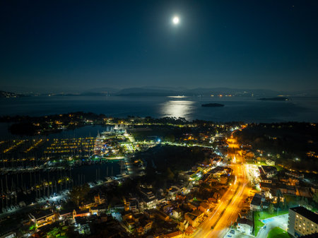 Aerial panoramic night view of Gouvia Marina in Corfu island, Greece, with bright city lights and a full moon over the Ionian Sea.の写真素材