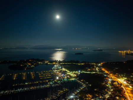 Night aerial view of a bright full moon rising over the calm sea and Gouvia Marina with illuminated yachts and sailboats docked at the piers in Corfu island, Greeceの写真素材