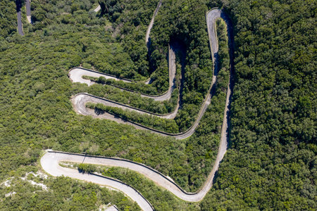 Aerial view of winding mountain road with hairpin turns through lush green forest in Sokraki, Corfu,...
