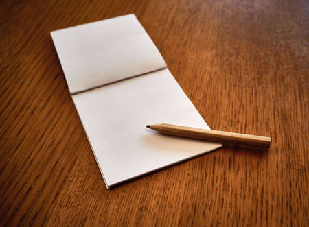 Empty notepad next to a pencil, on a wooden table