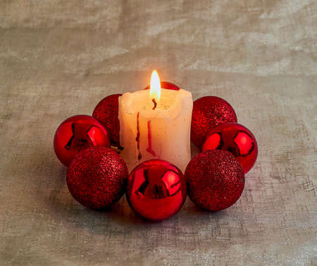 A lit candle surrounded by red Christmas ballsの写真素材