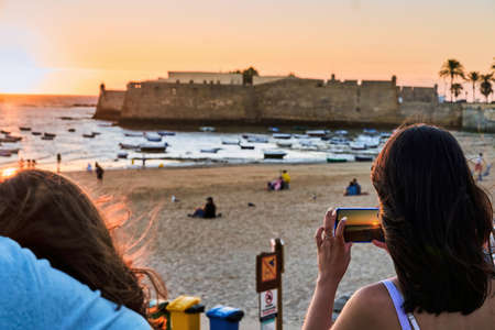 Woman recording with her cell phone, a beautiful sunset on the beach with a group of people, in summer.の写真素材