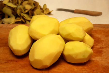 Peeled potatoes on a cutting board with peels and knife in the backgroundの写真素材