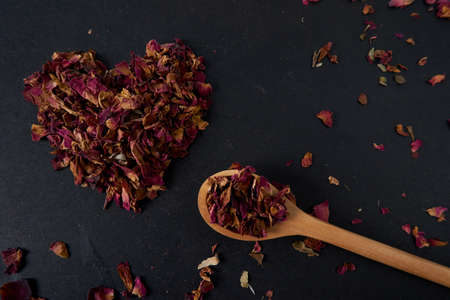 organic rose petals tea heart on black table with wooden spoonの写真素材