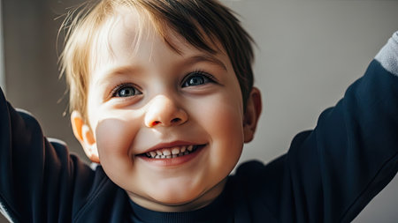 A young child is depicted with arms raised in a gesture of joy, showcasing a bright smile. The close-up captures clear facial features and bright eyes. The lighting suggests an indoor setting with potential uses in various commercial applications or editorial content.の素材