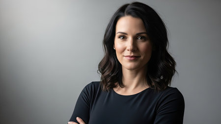 A headshot shows a woman with dark hair against a gray backdrop. She is looking directly at the camera with a subtle expression. The lighting is soft and even. This image could be used for various commercial or editorial purposes, such as websites or brochures.の素材