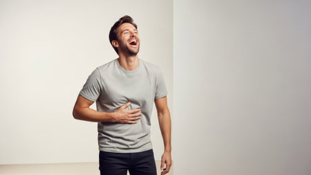 A man laughs with his head back, hand on his stomach, in a studio setting. The image uses a neutral background with soft lighting. The composition features a full body shot. This image could be suitable for various commercial projects related to joy, happiness, or lifestyle themes.の素材