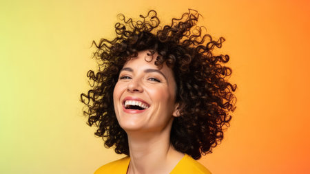 A woman with dark, curly hair smiles broadly, her face radiating happiness. Set against a warm gradient background of yellow and orange, the portrait features bright lighting and a shallow depth of field. This image is suitable for various uses, including editorial and commercial projects that require positive emotions.の素材