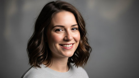 A woman with short brown hair smiles in a studio portrait. The image features soft lighting and a neutral gray backdrop emphasizing the subject. This professional headshot is suitable for various commercial uses, including advertising and editorial content.の素材