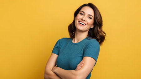 A woman stands with arms crossed, smiling broadly against a solid yellow backdrop. She has brown hair and is wearing a blue shirt. The image has a studio lighting and a clean composition. This portrait is suitable for various commercial applications, including advertising and editorial content.の素材