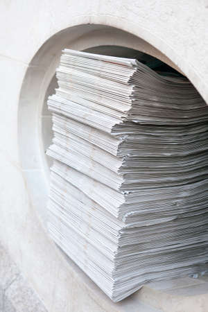Many fresh newspapers stacked in a pile in a hole for newspaperの写真素材