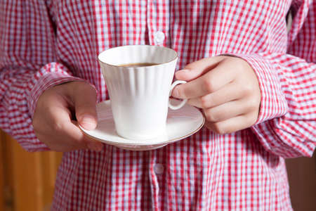 Woman in a red white shirt holding a white cup with two hands close upの写真素材