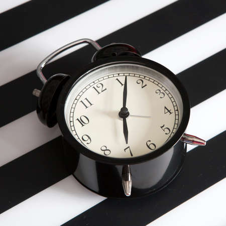 the Black alarm clock on a black and white striped napkin showing 7 o'clock on a bedside table