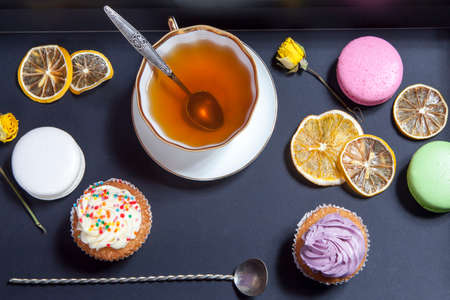 Tea in a cup and saucer, dried yellow roses, cake on a black background. Afternoon tea.の写真素材
