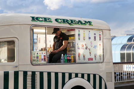 LONDON, UK - August 27, 2016: The seller of ice cream in the car for selling ice-cream and coca-cola waiting for customers, while reading the news in his phone on the Southbank of the Thames.のeditorial素材