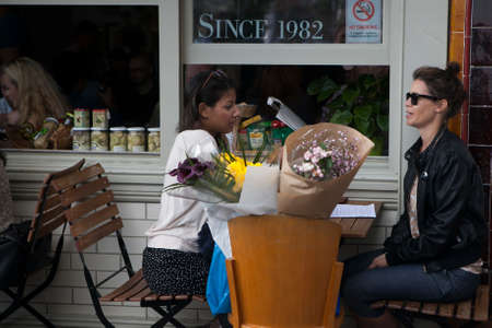 LONDON, ENGLAND - JULY 12, 2016 The two women bought flowers in the Columbia road flower market, sitting at an outdoor cafe, talkingのeditorial素材