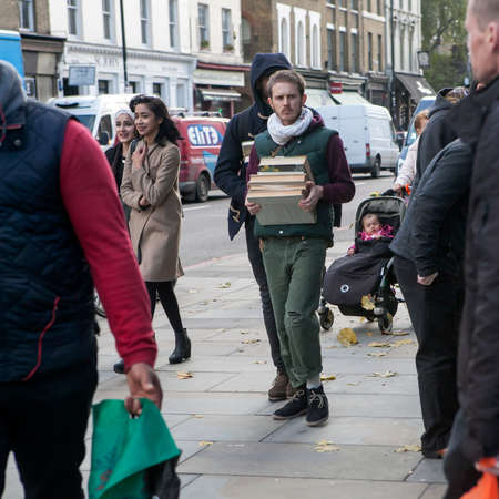 LONDON, UK - APRIL 22, 2016: serious man carries a stack of books on Brick Laneのeditorial素材