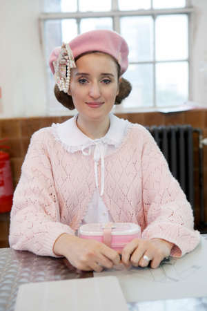 LONDON, UK - APRIL 22, 2016: Model in a pink sweater and a pink beret with make-up posing while sitting at the table.のeditorial素材