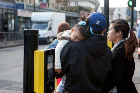 LONDON, ENGLAND - JULY 12, 2016 Asian kid girl sleeping on the shoulder of the father. Crosswalk, people are waiting for the traffic light signalのeditorial素材