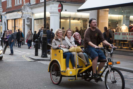 LONDON, UK - 16TH MARCH 2016: A man riding a Rickshaw with happy women in the back down a street in Londonのeditorial素材