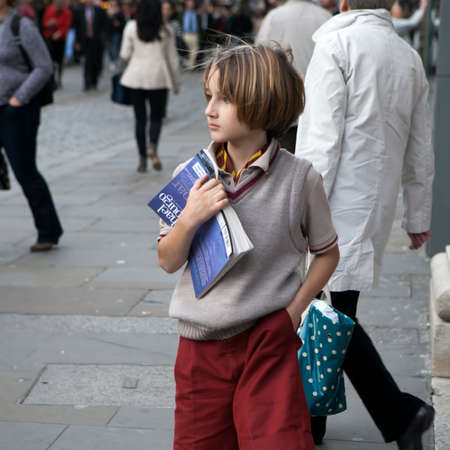 LONDON, ENGLAND - JULY 12, 2016 A fashionable boy of ten years in burgundy shorts and a beige vest stands on the street, pressing the book to his chestのeditorial素材