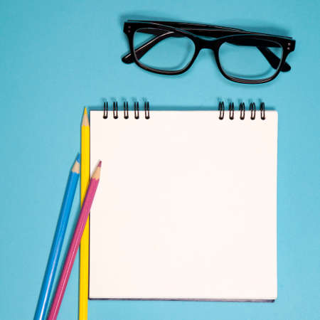 White notebook on springs, glasses and colored pencils on a blue background. Copyspaceの写真素材
