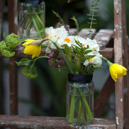A bouquet of narcissus, carnations, eucalyptus, fern and hydrangea in a glass jarの写真素材