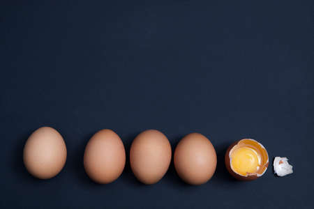 Whole eggs with one broken in a row on a gray background