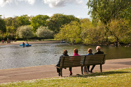 LONDON, ENGLAND - JULY 12, 2016 Four pensioners sit on a bench, admiring the lake in Victoria Park.のeditorial素材