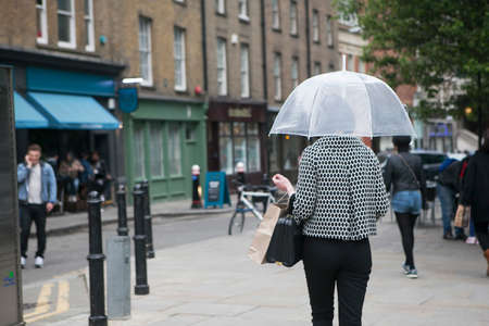 LONDON, ENGLAND - JULY 12, 2016 A girl in a black and white plaid fashion jacket under a transparent umbrella against the backdrop of Londonのeditorial素材