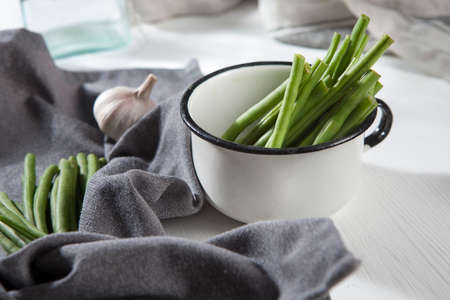 Green beans in an aluminum cup, napkin and garlic on a white wooden table. Autumn recipes. Copy spaceの写真素材