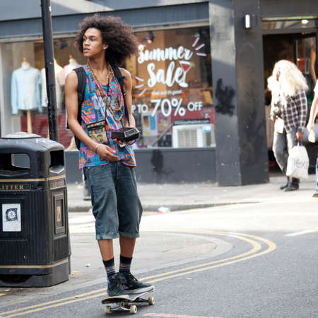 LONDON, ENGLAND - August 22, 2017 A young man on a skateboard with a box for food in his hand turns to another streetのeditorial素材
