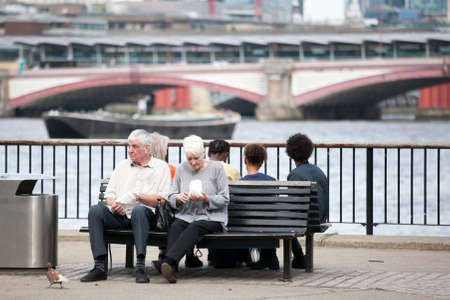 LONDON, ENGLAND - August 11 2017 An elderly couple eating popcorn, sitting on a bench overlooking the Thames. South Shore of the Thamesのeditorial素材