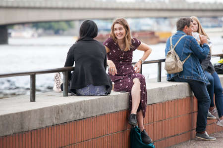 LONDON, ENGLAND - August 11 2017 Girls are sitting on the parapet by the river, talking and laughingのeditorial素材