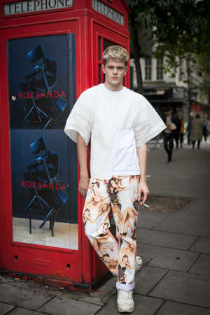 LONDON, ENGLAND - September 15, 2017 Beautiful and stylish young man in white T-shirt and colored brown training pants in front of red telephone booth. posing during the London Fashion Week. outside Eudon Choiのeditorial素材
