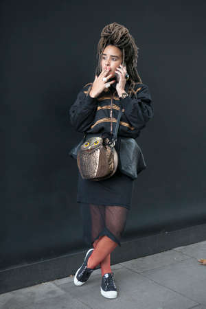 LONDON, ENGLAND - September 15, 2017 A woman with dreadlocks, a tattoo in front of her eyes, in a black leather jacket, a bag in the shape of an owl talking on the phone during the London Fashion Week. outside Eudon Choiのeditorial素材