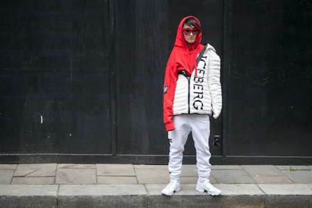 LONDON, ENGLAND - September 15, 2017 A young girl in a red hoodie, glasses and a white sports jacket firm Iceberg poses in front of black wall during the London Fashion Week. outside Eudon Choiのeditorial素材