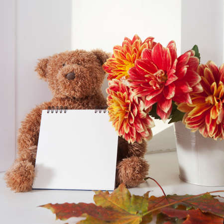 A teddy-bear next to bouquet of autumn dahlias. The teddy-bear holds a notepad for writing.の写真素材