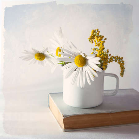 Daisies in a white enamel mug on white paper background. Vintage backgroundの写真素材