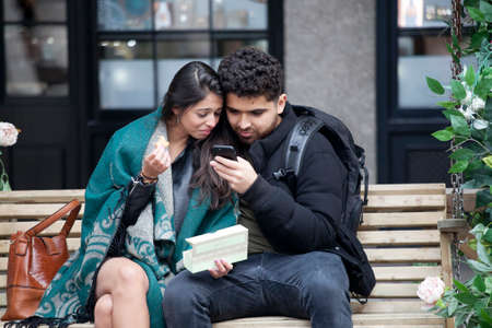 LONDON, ENGLAND - September 11, 2017 Happy couples look in the phones, sitting on a bench near Covent Gardenのeditorial素材
