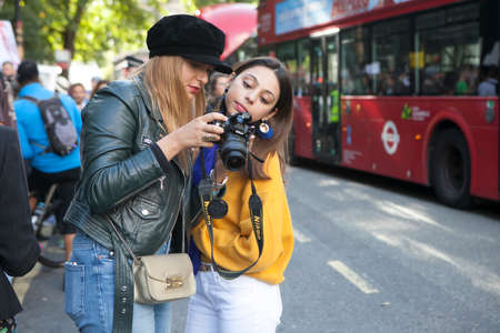 LONDON, ENGLAND - September 15, 2017 Beautiful and stylish Two girls in a yellow sweater examine a photo in the phone during the London Fashion Week.のeditorial素材