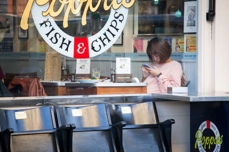 London, UK - December 22, 2017: girl in a pink sweater at a table in a cafe looks into her phone...